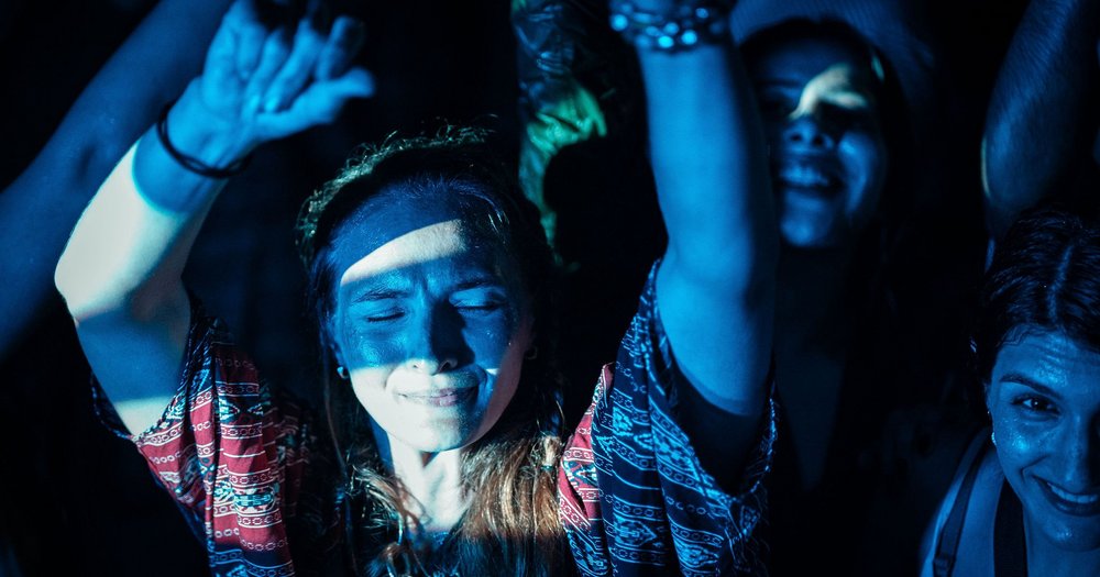 A group of people in a dark room with their hands raised, conveying an atmosphere of tension or celebration.