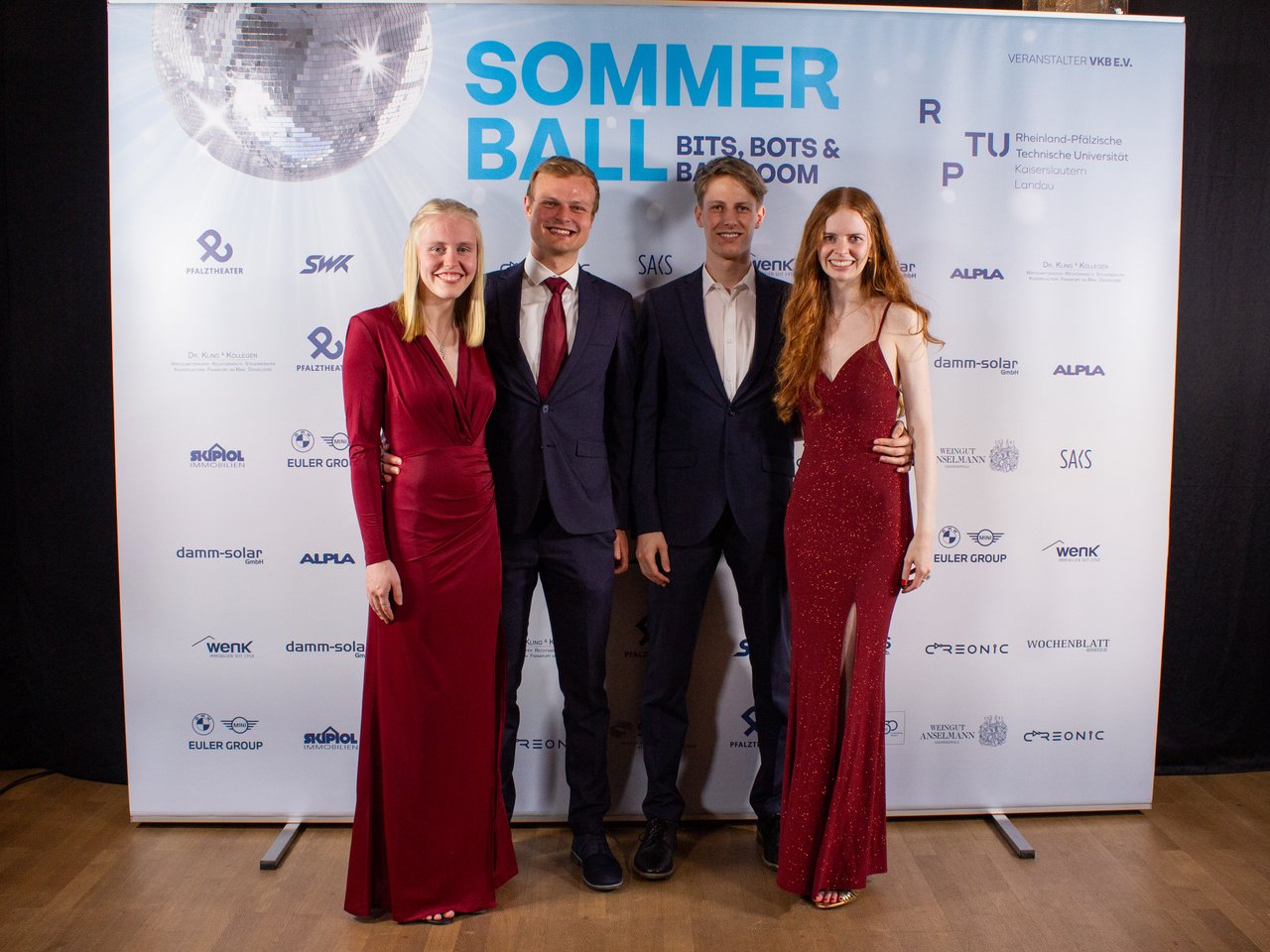 Des personnes posent devant une bannière portant l'inscription 'Sommer Ball'.
