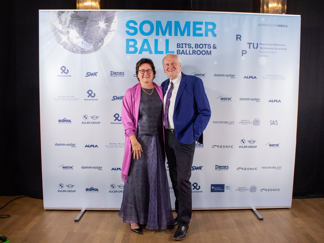 Des personnes posent devant une bannière portant l'inscription 'Sommer Ball'.
